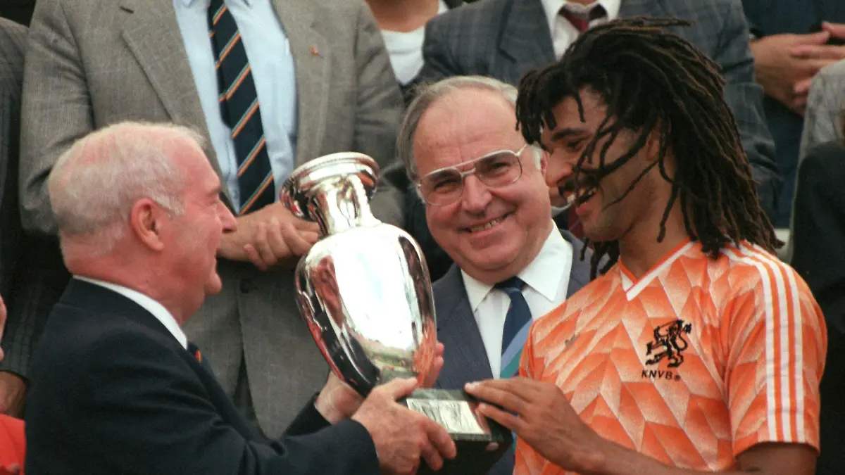ARCHIV - 25.06.1988, Bayern, München: Der niederländische Stürmer Ruud Gullit (r) empängt den Europameisterpokal aus den Händen des französischen UEFA-Präsidenten Jacques Georges (l), und Bundeskanzler Helmut Kohl (M) schaut lächelnd zu. Die niederländische Fußballnationalmannschaft besiegt am 25.6.1988 im Endspiel des EM-Turniers im Münchner Olympiastadion die Elf der UdSSR mit 2:0. 25 Jahre später muss sie um die Teilnahme an der EM 2024 bangen. (zu dpa: «Feuriger Abend in Athen: Oranje nach Frankreich-Pleite unter Druck») Foto: - +++ dpa-Bildfunk +++