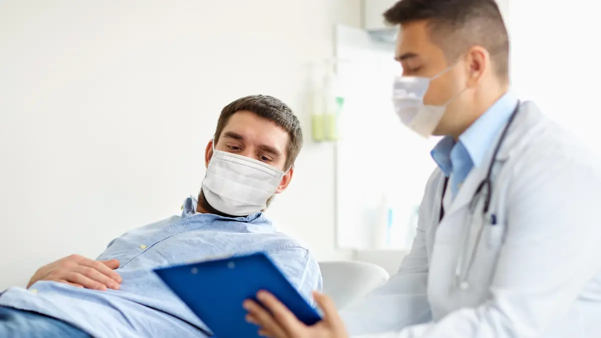 medicine, healthcare and pandemic concept - doctor wearing face protective medical mask for protection from virus disease with clipboard and young male patient at medical exam at hospital