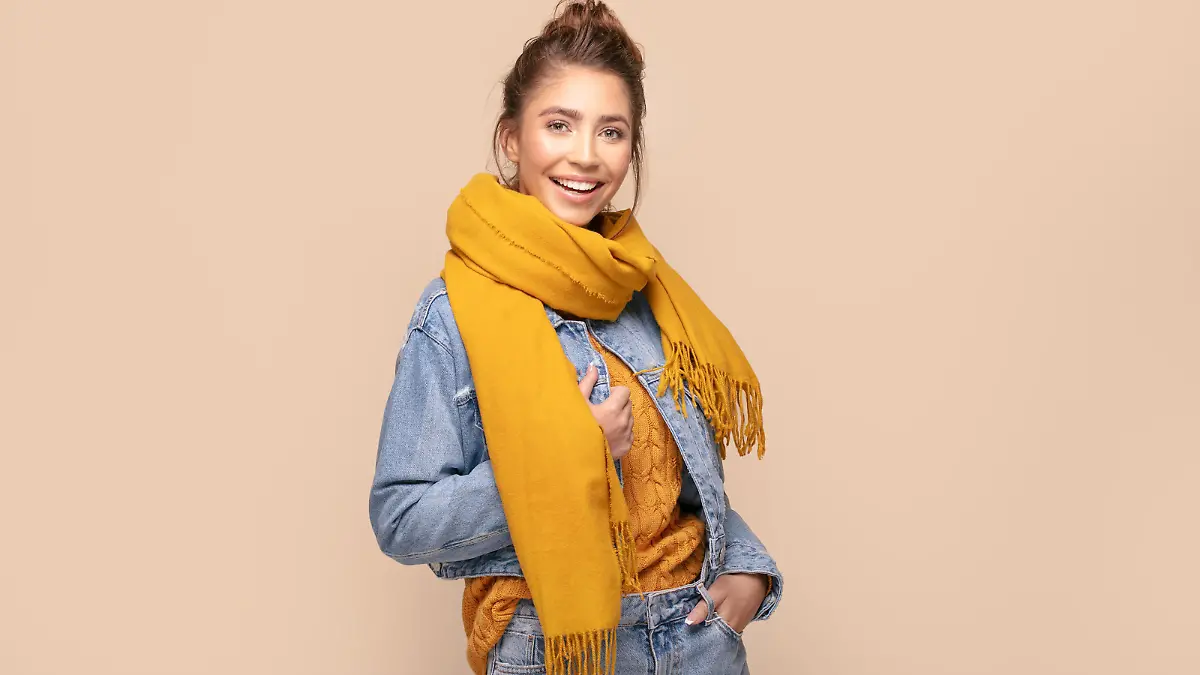 Young beautiful happy girl posing in studio wearing fashionable scarf and jeans jacket. Smiling woman looking at camera. Human emotions,, expression. Beige studio background.