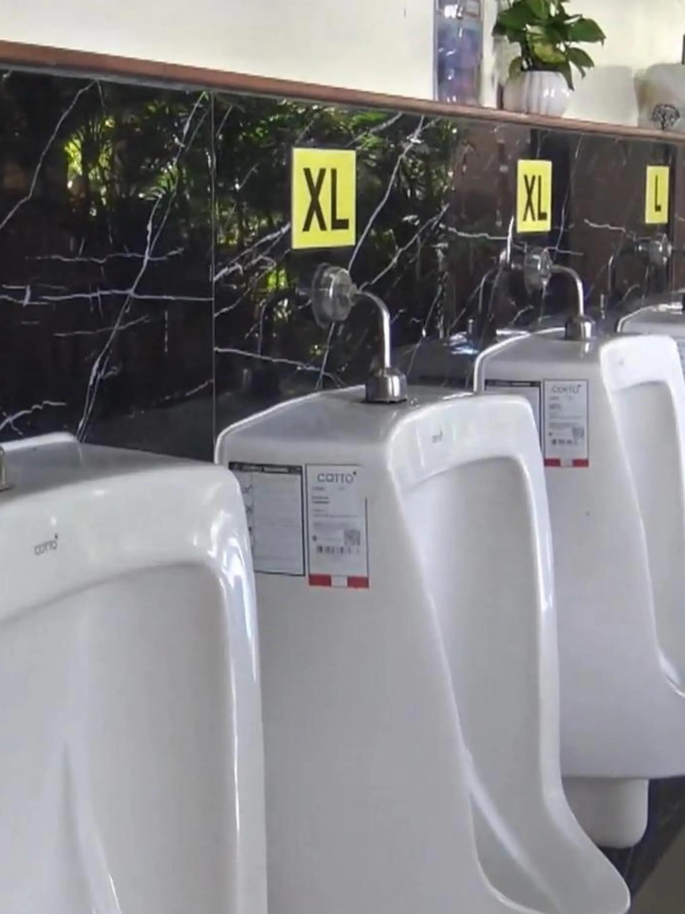 Wer hat denn hier den Längsten? Diese Frage scheinen Schilder auf einer Autobahnraststätte in Thailand klären zu wollen. Die Betreiberin hat ihre Urinale mit Stickern versehen – von super small bis XXL. Werden die Toilettenplätze hier etwa nach Penisgröße vergeben?