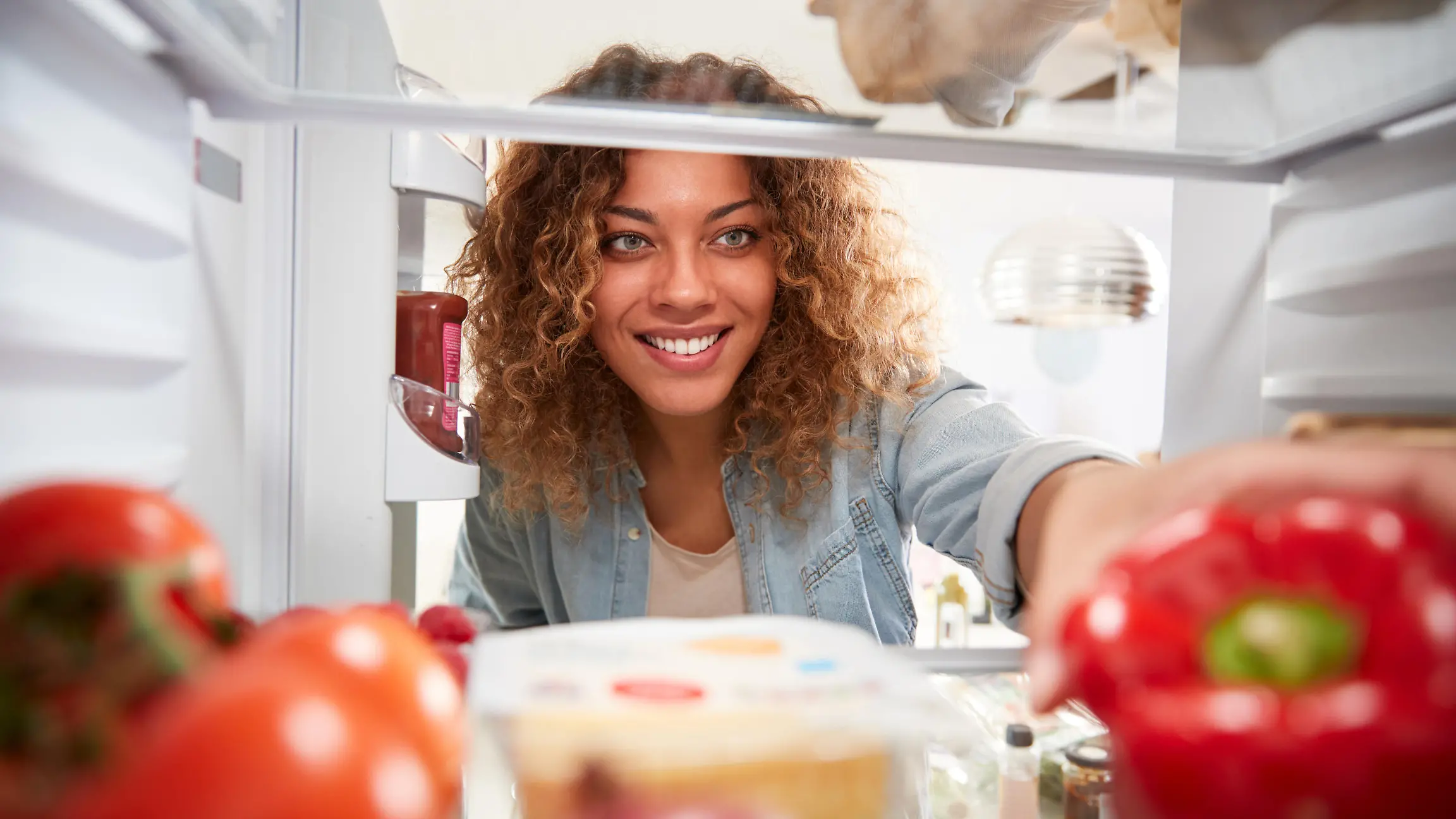View Looking Out From Inside Of Refrigerator As Woman Opens Door And Unpacks Shopping Bag Of Food