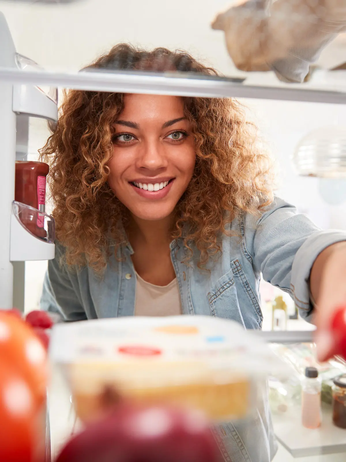 View Looking Out From Inside Of Refrigerator As Woman Opens Door And Unpacks Shopping Bag Of Food