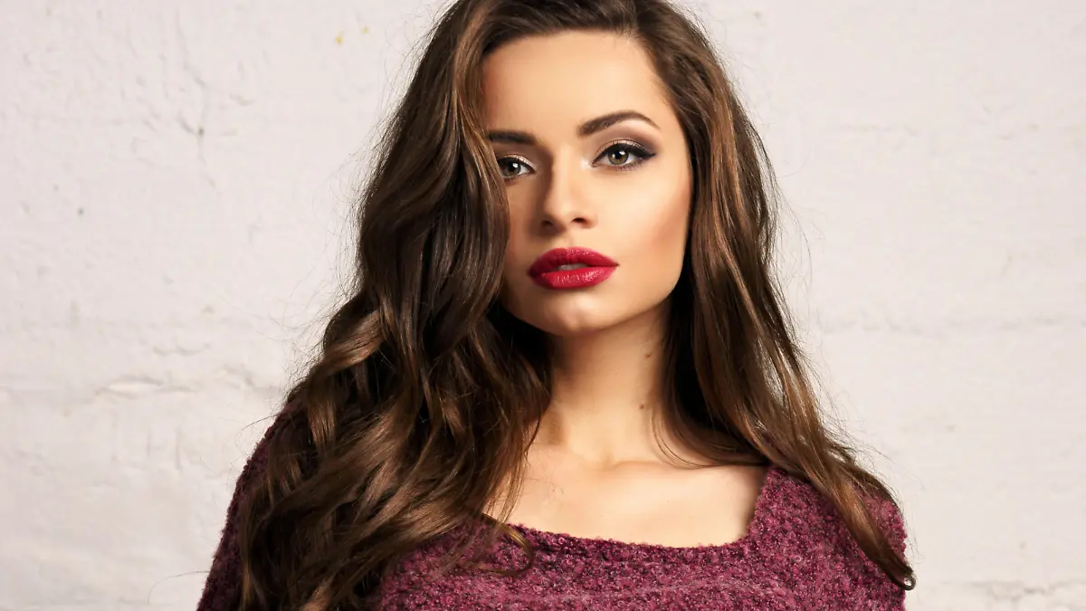 Young beautiful gorgeous female model inpurple pullover posing against white brick wall. Stunning glamorous girl with long curly hair