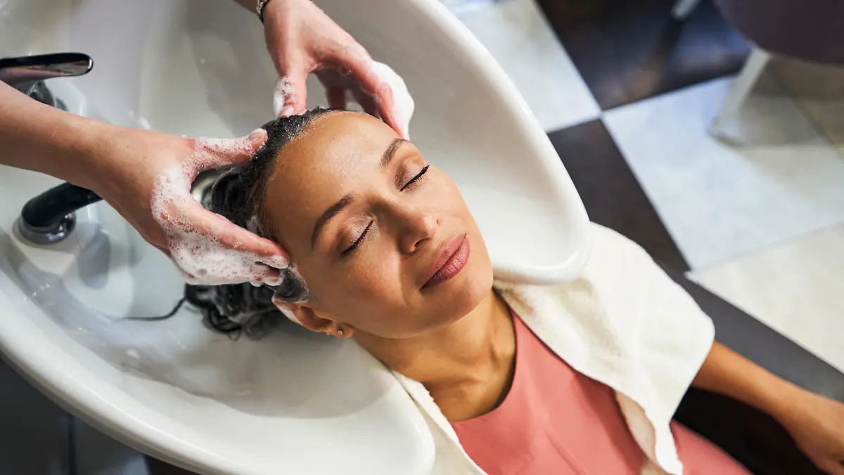 Relaxed international woman closing her eyes while hairdresser washing her hair
