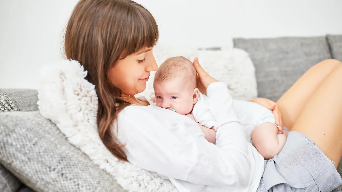 Mutter schmust liebevoll mit ihrem neugeborenen Baby auf dem Sofa || Modellfreigabe vorhanden