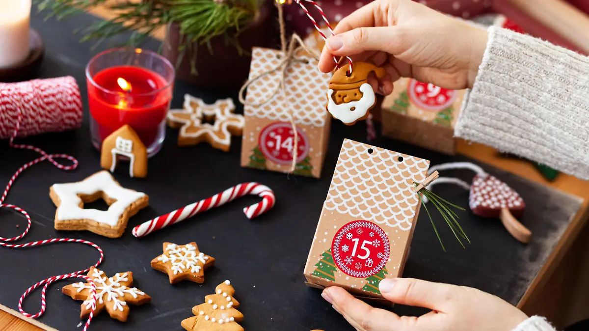 Woman preparing original Advent holiday calendar for Christmas or New year as countdown to Christmas Eve for kids. Zero waste paper package, homemade gingerbread cookies. Cozy home atmosphere