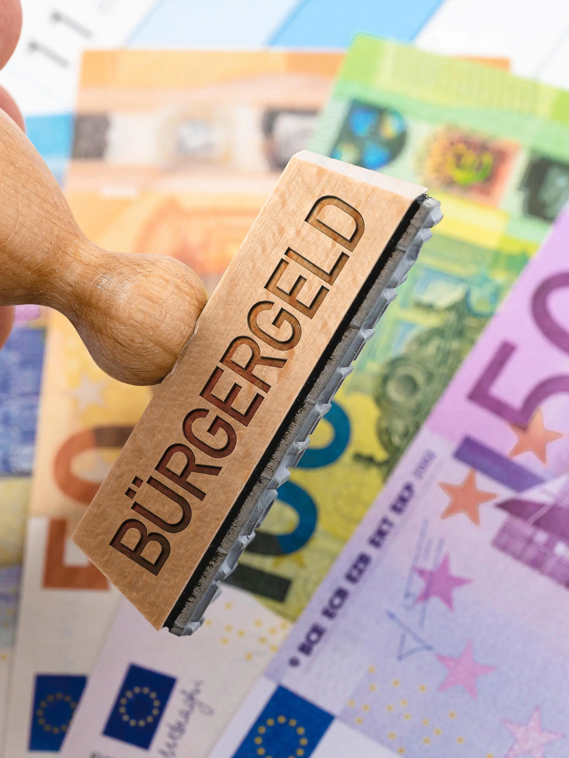  Deutschland - 05 August 2022: Stamp made of wood with the inscription: Citizen money, Hartz 4 successor, new social welfare for the unemployed in Germany, banknotes on a calendar PHOTOMONTAGE *** Stempel aus Holz mit der Aufschrift: Bürgergeld, Hartz 4 Nachfolger, neue Sozialhilfe für Arbeitslose in Deutschland, Geldscheine auf einem Kalender FOTOMONTAGE