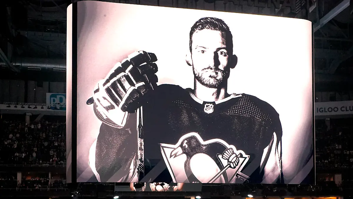 The Pittsburgh Penguins and Anaheim Ducks gather at center ice, before an NHL hockey game in Pittsburgh, Monday, Oct. 30, 2023, to honor former Penguin player Adam Johnson, shown on the scoreboard, who died in a "freak accident" while playing in an English hockey league game. (AP Photo/Gene J. Puskar)