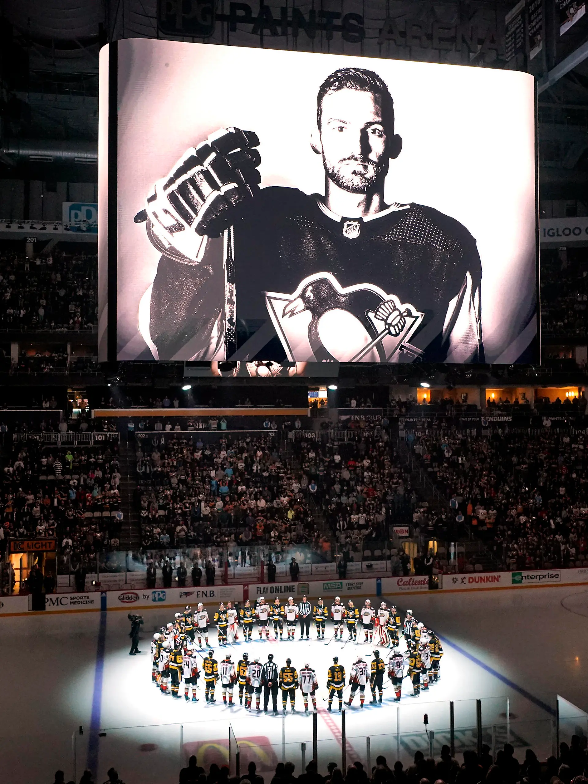 The Pittsburgh Penguins and Anaheim Ducks gather at center ice, before an NHL hockey game in Pittsburgh, Monday, Oct. 30, 2023, to honor former Penguin player Adam Johnson, shown on the scoreboard, who died in a "freak accident" while playing in an English hockey league game. (AP Photo/Gene J. Puskar)