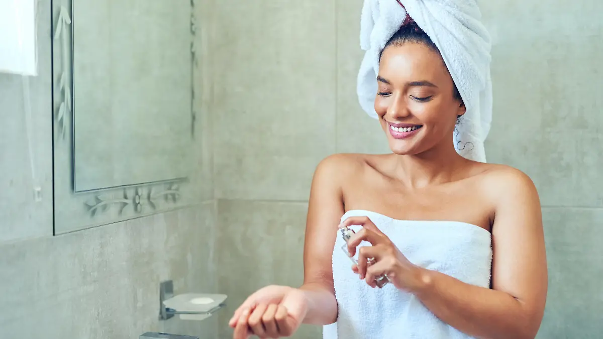 Cropped shot of a young woman spraying perfume after washing