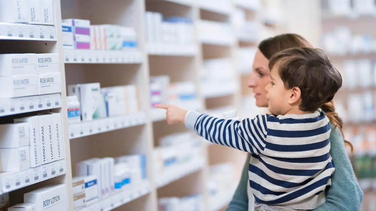 Son pointing to medicine bottle while mother carrying him in her arms in drugstore.