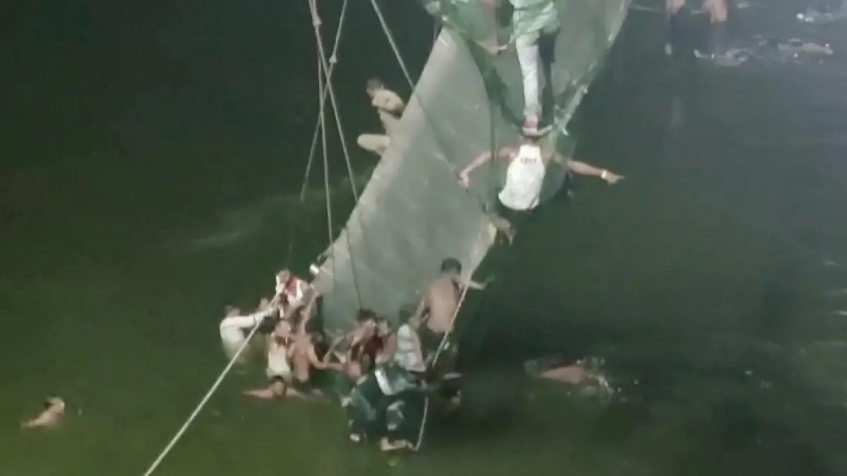 People cling on to the collapsed suspension bridge in Morbi, India October 30, 2022 in this screen grab obtained from a video. ANI/ Handout via REUTERS THIS IMAGE HAS BEEN SUPPLIED BY A THIRD PARTY INDIA OUT. NO COMMERCIAL OR EDITORIAL SALES IN INDIA
