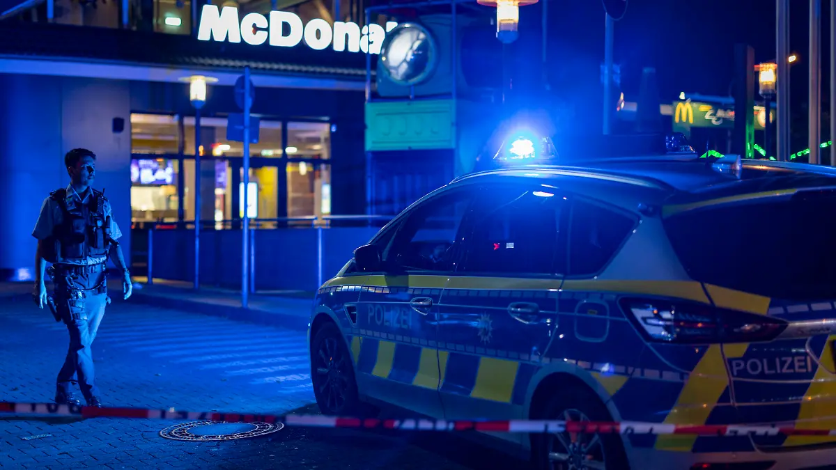 29.10.2022, Nordrhein-Westfalen, Oberhausen: Ein Polizist geht vor einem Fast-Food-Restaurant im Blaulicht, nachdem im Außenbereich Schüsse gefallen waren. Drei Menschen wurden verletzt. Der Täter sei auf der Flucht, teilte ein Polizeisprecher mit. Die Hintergründe der Tat sind dem Sprecher zufolge noch unklar. Foto: Christoph Reichwein/dpa +++ dpa-Bildfunk +++
