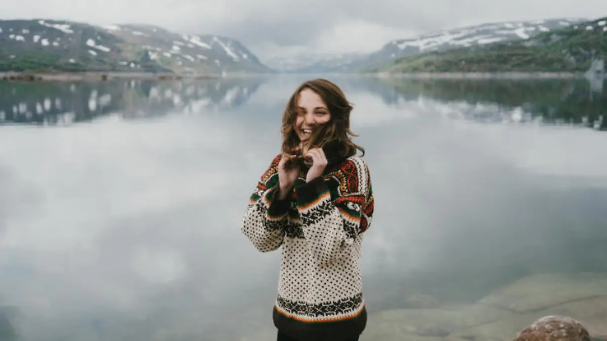 Young Caucasian woman in knitted sweater  laughing near the  fjord in Norway