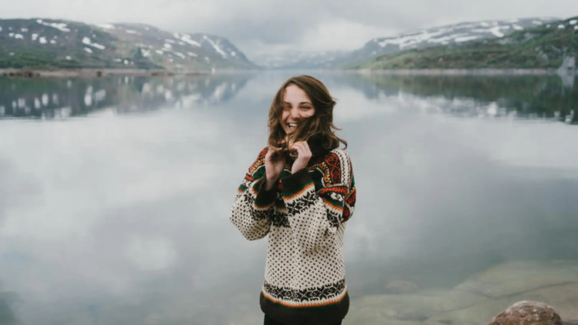 Young Caucasian woman in knitted sweater laughing near the fjord in Norway