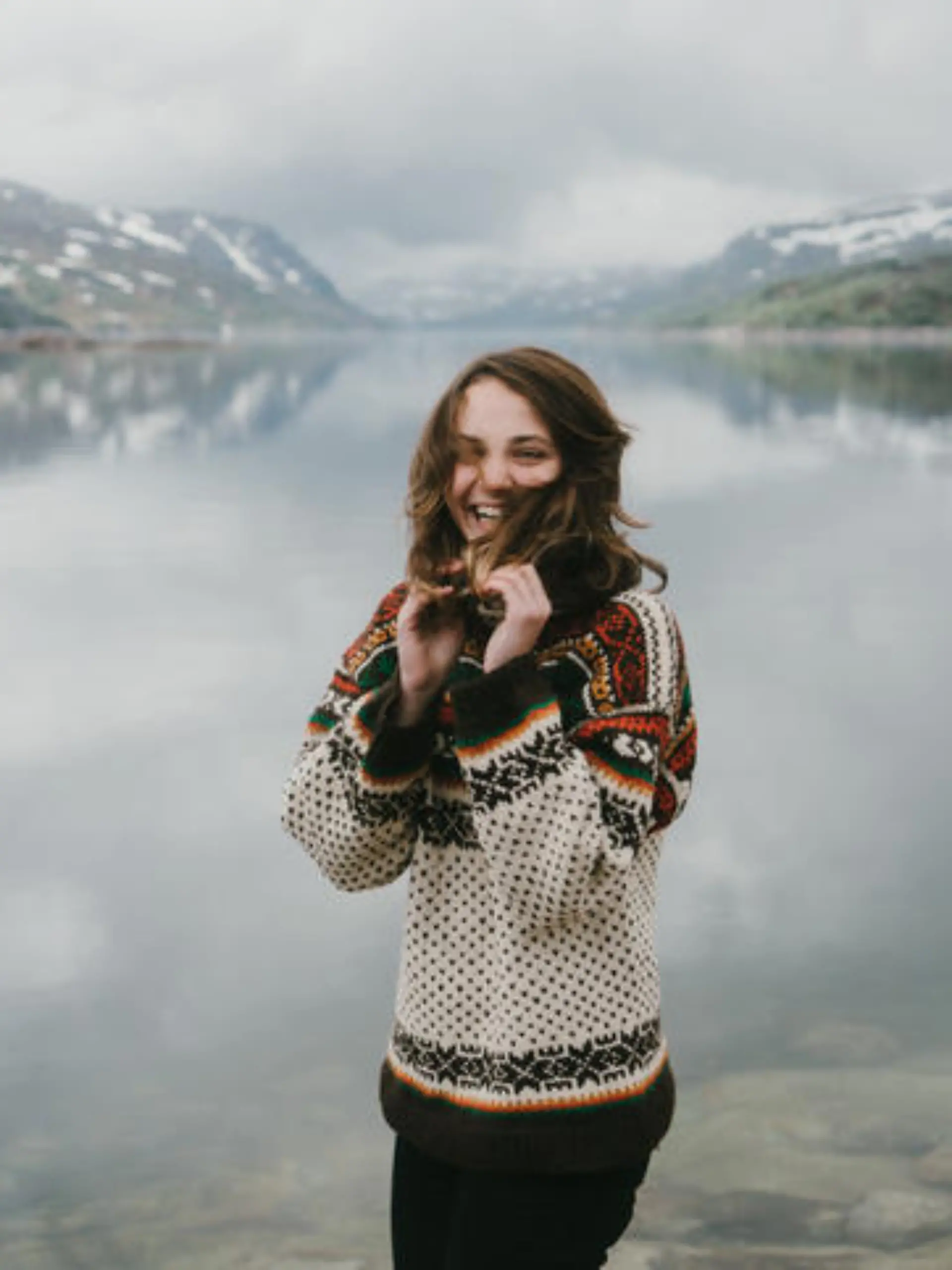 Young Caucasian woman in knitted sweater laughing near the fjord in Norway