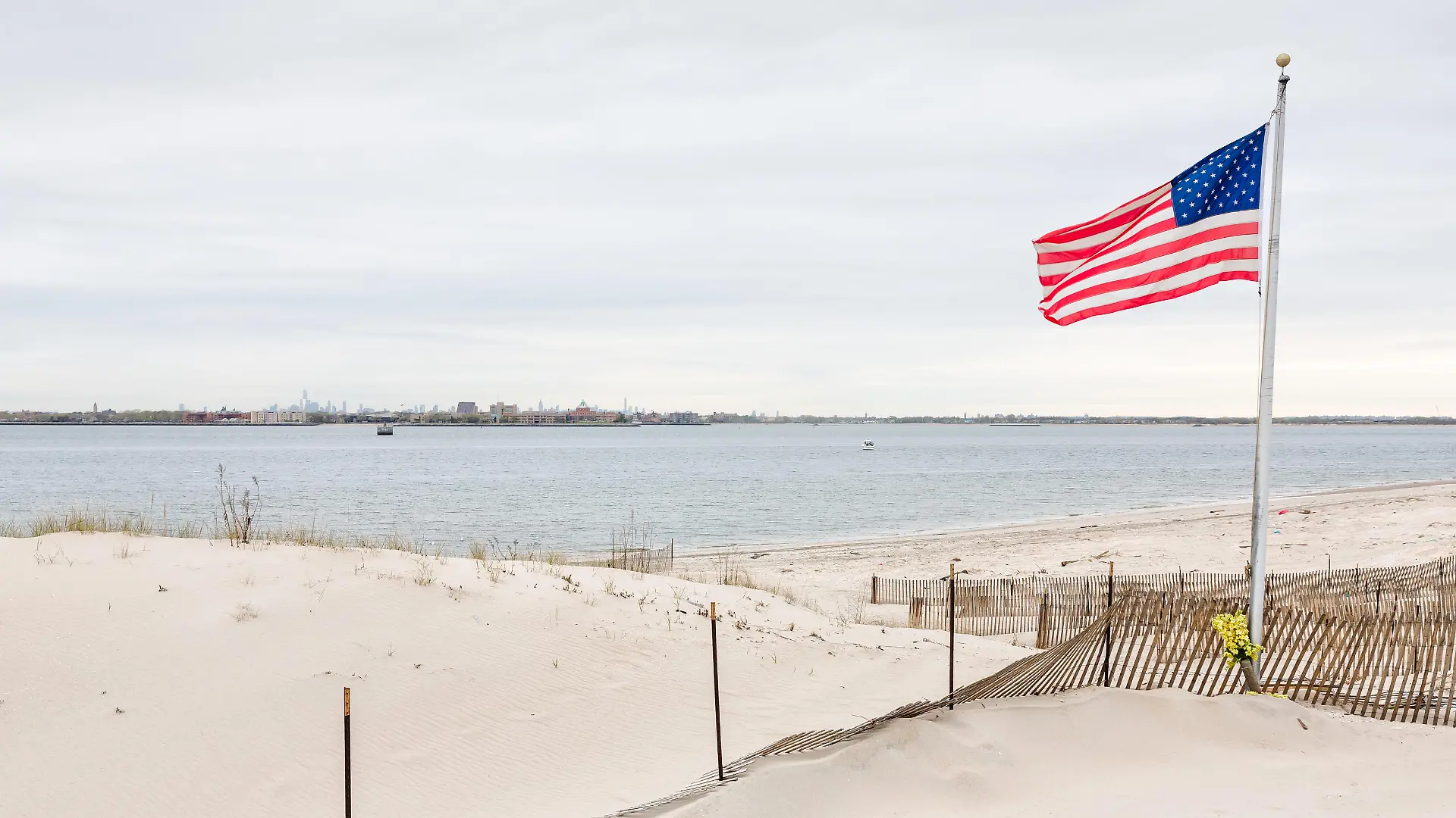 American flag on the beach of Breezy Point. Breezy Point is a neighborhood in the New York City borough of Queens, located on the western end of the Rockaway peninsula. Manhattan in the background xkwx 9/11, america american, beach, breezy, city, flag, manhattan, memorial, morning, neighborhood, new, nY, nYC, ocean, peninsula, point, queens, rockaway, us, usa, york, beach, Coast, sandy, sky, gulf, bay