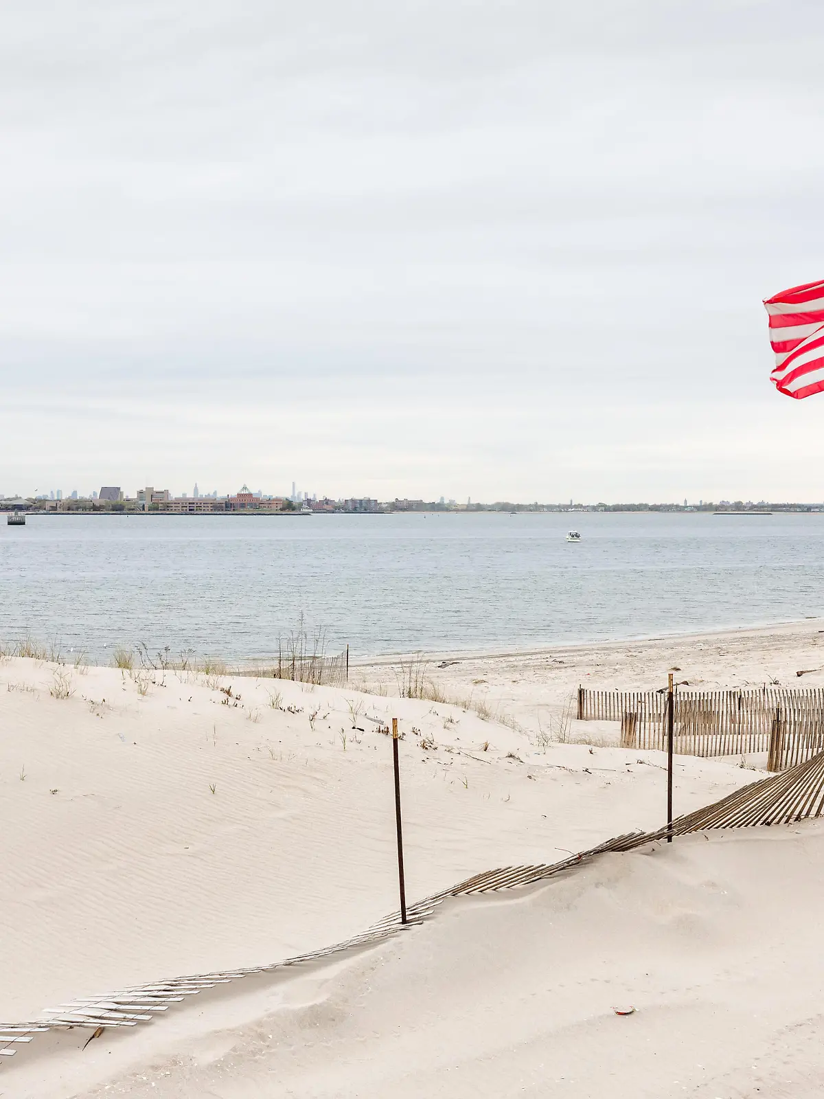 American  flag  on  the  beach  of  Breezy  Point.  Breezy  Point  is  a  neighborhood  in  the  New  York  City  borough  of  Queens,  located  on  the  western  end  of  the  Rockaway  peninsula.  Manhattan  in  the  background xkwx 9/11,  america  american,  beach,  breezy,  city,  flag,  manhattan,  memorial,  morning,  neighborhood,  new,  nY,  nYC,  ocean,  peninsula,  point,  queens,  rockaway,  us,  usa,  york,  beach,  Coast,  sandy,  sky,  gulf,  bay