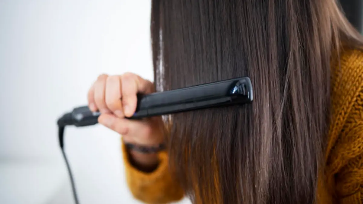 Unrecognizable woman using hair straightener.