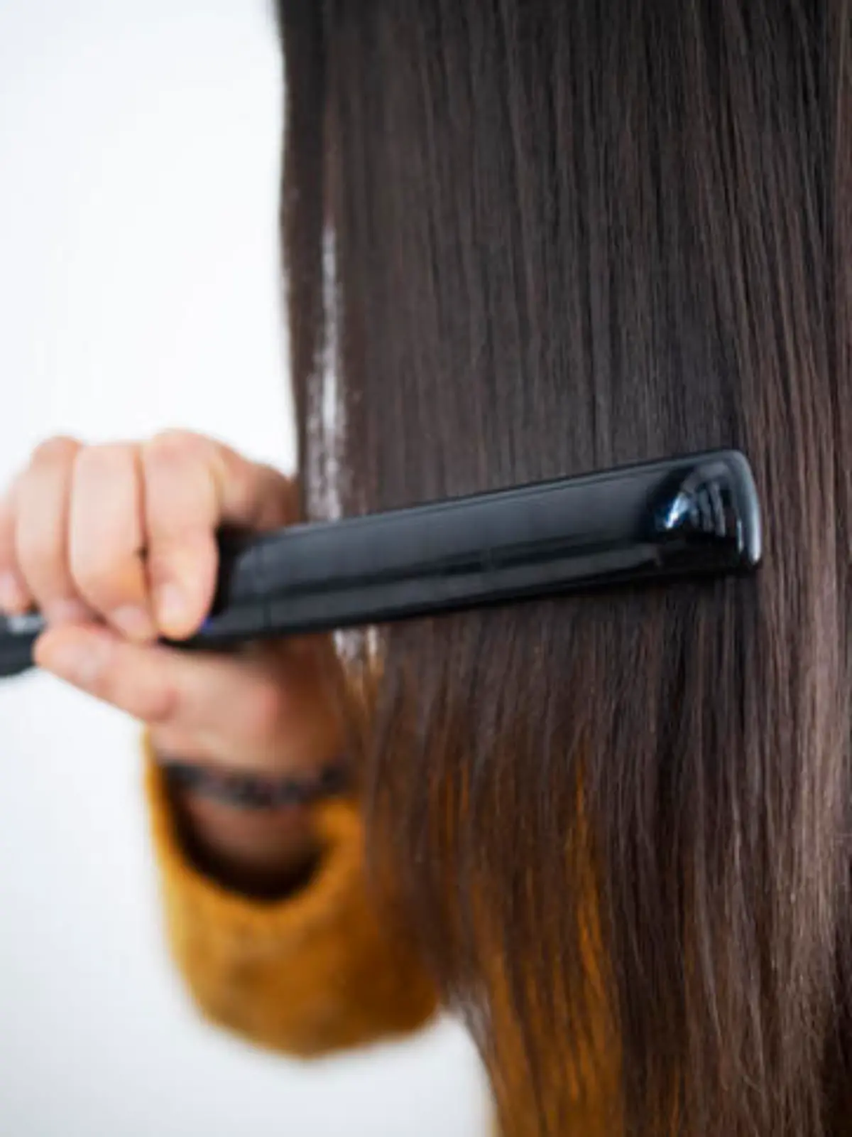 Unrecognizable woman using hair straightener.