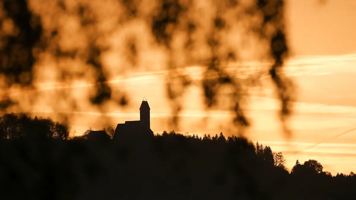 28.10.2022, Baden-Württemberg, Riedlingen: Hinter dem Berg Bussen mit seiner Wallfahrtskirche hat sich am Morgen der Himmel durch die Sonne und Saharastaub, der in der Luft liegt, gelblich gefärbt. Foto: Thomas Warnack/dpa +++ dpa-Bildfunk +++