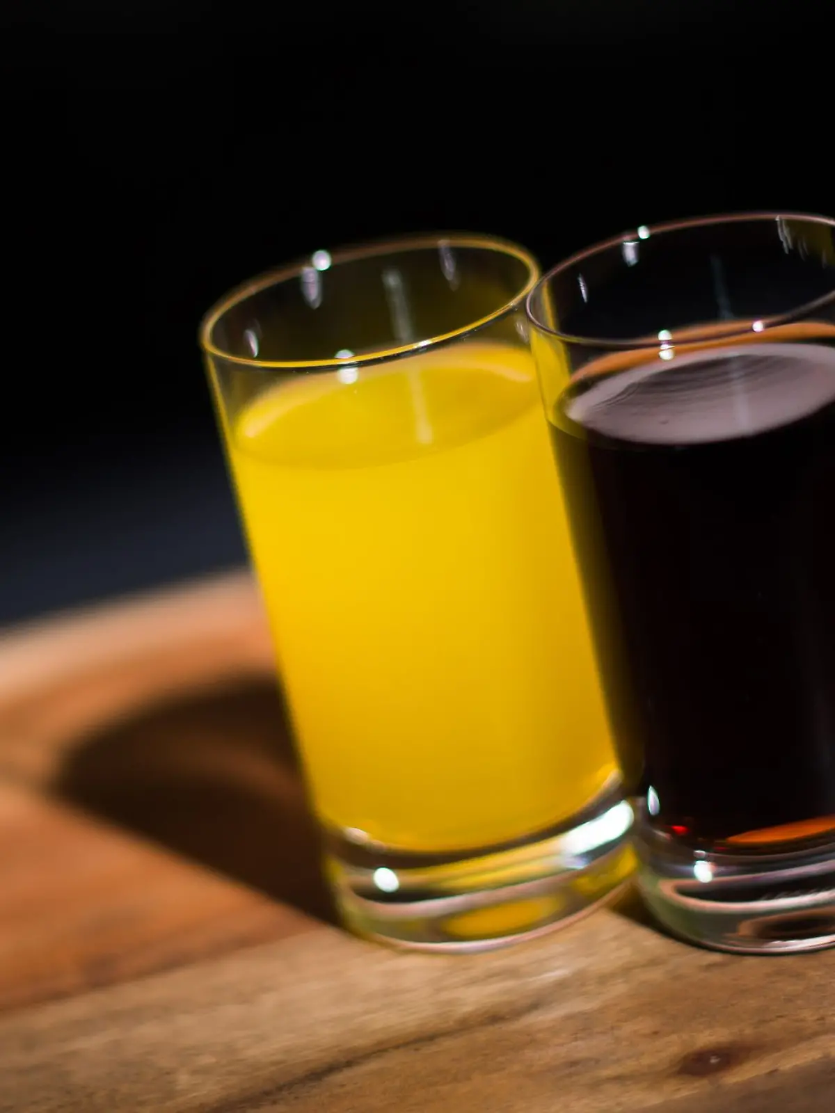 Ein Glas mit Orangenlimo und ein Glas Cola stehen auf einem Tisch.