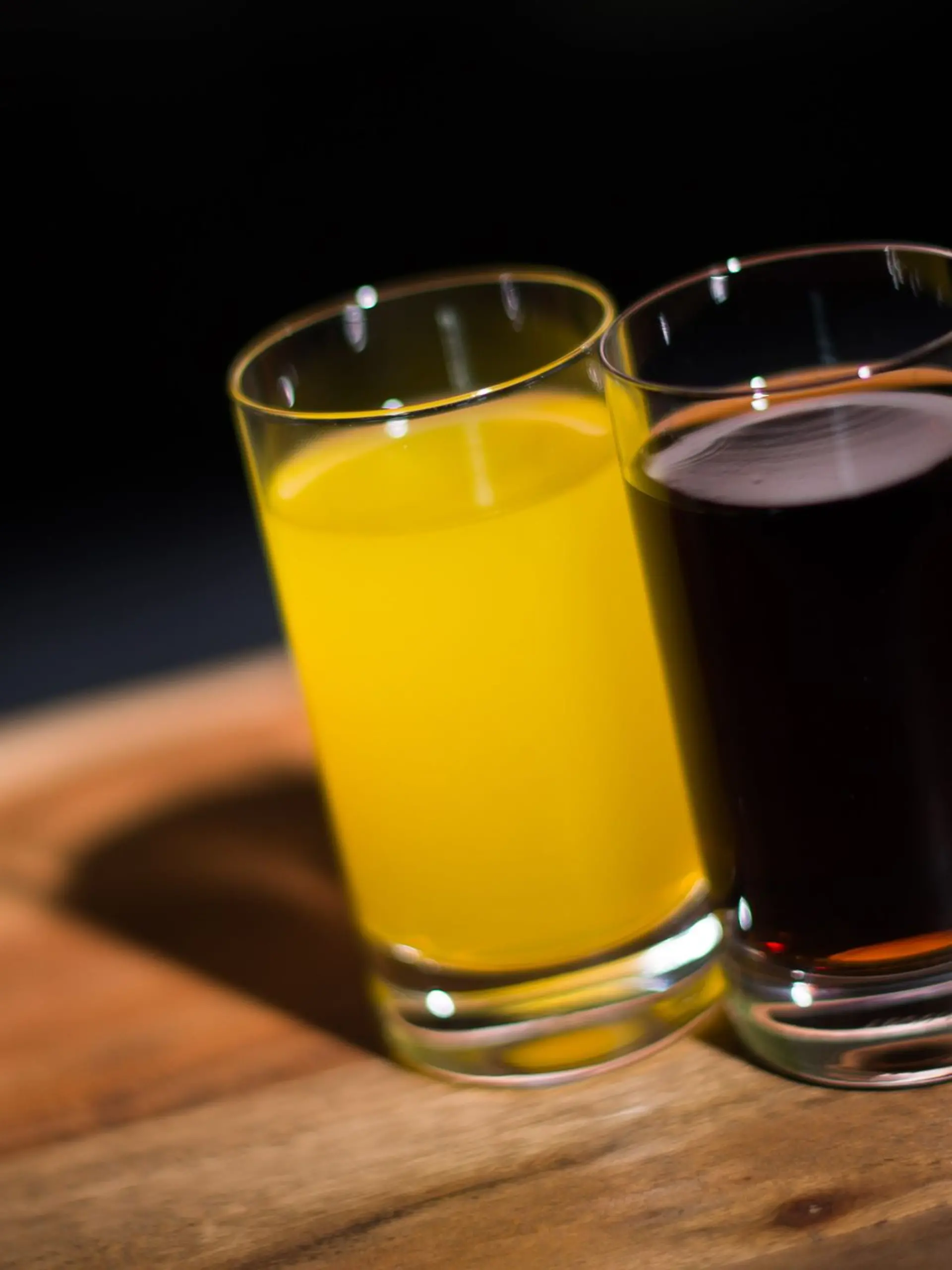 Ein Glas mit Orangenlimo und ein Glas Cola stehen auf einem Tisch.