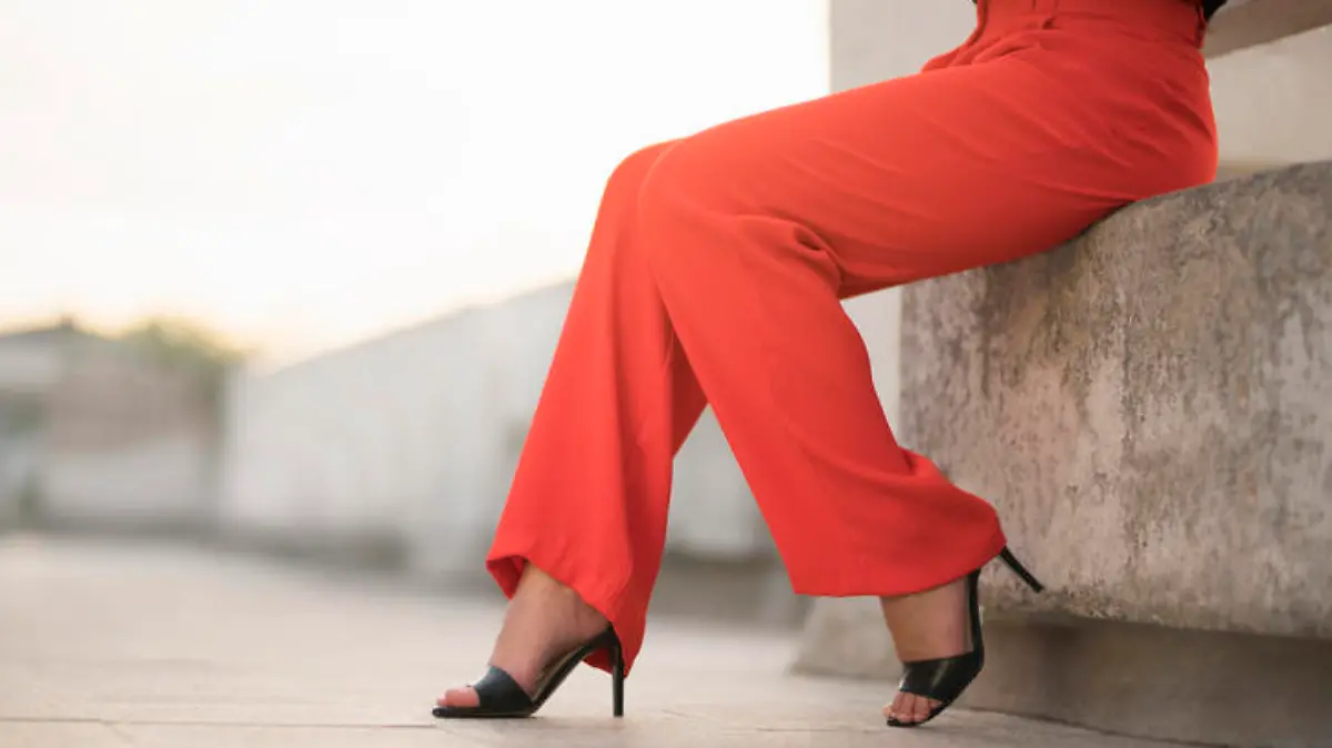 Fashion portrait of an unrecognizable young woman sitting at the balcony in red trousers and high heels; cut out.