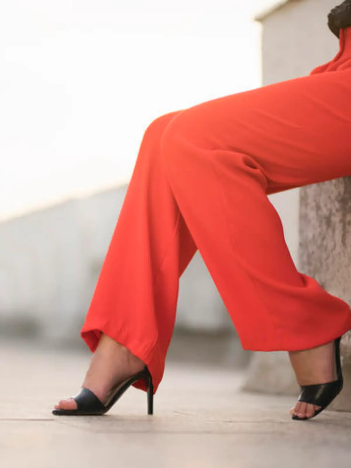 Fashion portrait of an unrecognizable young woman sitting at the balcony in red trousers and high heels; cut out.