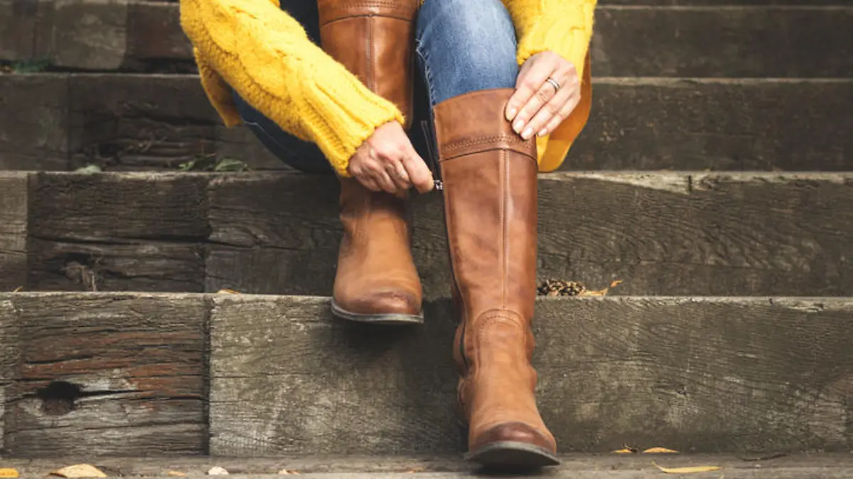 Woman sitting on stairs and fasten zipper on her leather boots. Autumn fashion concept