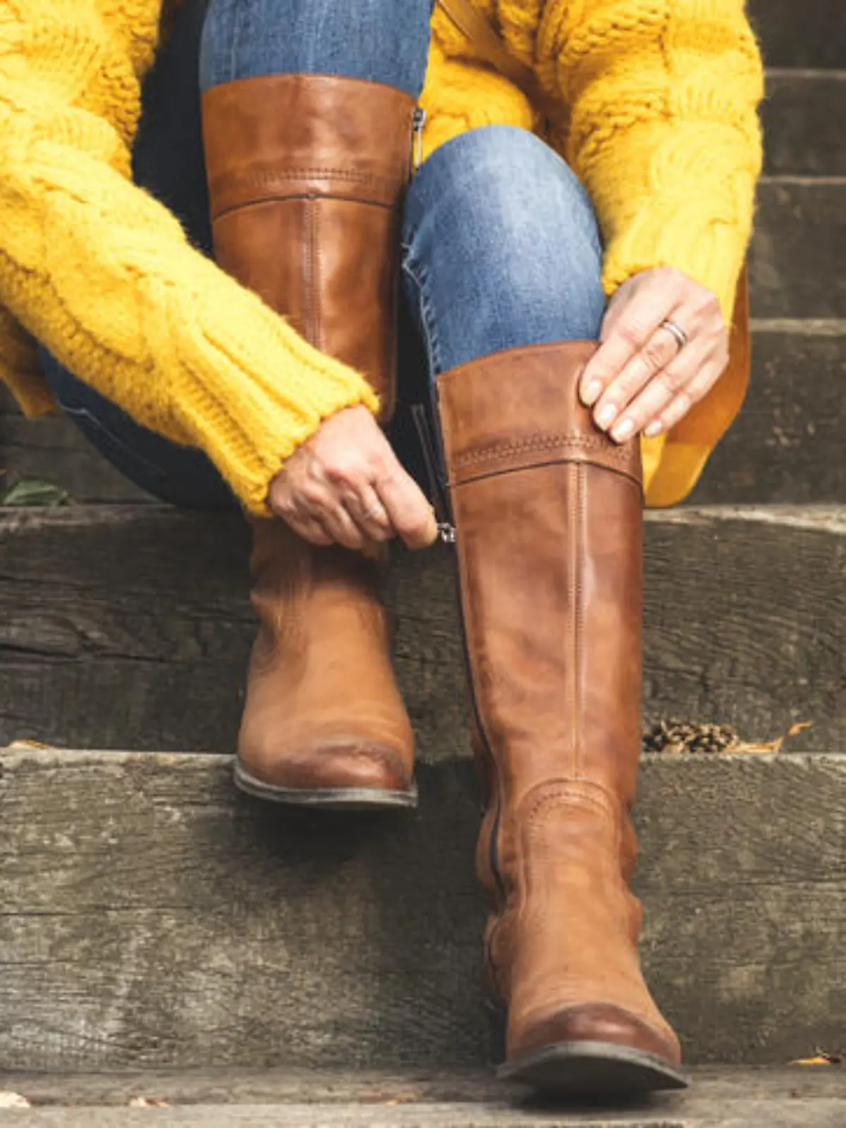 Woman sitting on stairs and fasten zipper on her leather boots. Autumn fashion concept