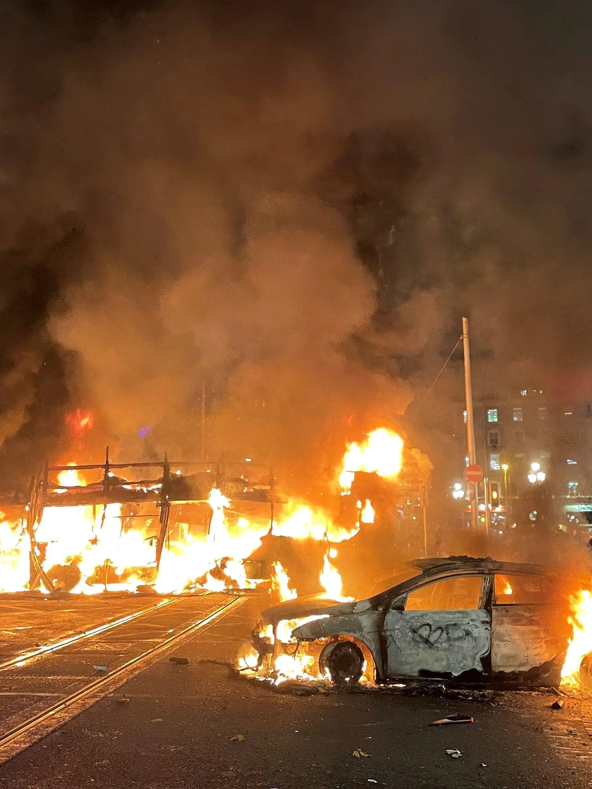 23.11.2023, Irland, Dublin: Ein Bus und ein Auto brennen in der O'Connell Street im Stadtzentrum von Dublin. Nach einem Messerangriff in der irischen Hauptstadt, bei dem unter anderem ein fünfjähriges Mädchen und eine Frau schwer verletzt wurden, kam es am Abend in der Nähe des Tatorts zu schweren Ausschreitungen. Foto: Brian Lawless/PA Wire/dpa +++ dpa-Bildfunk +++