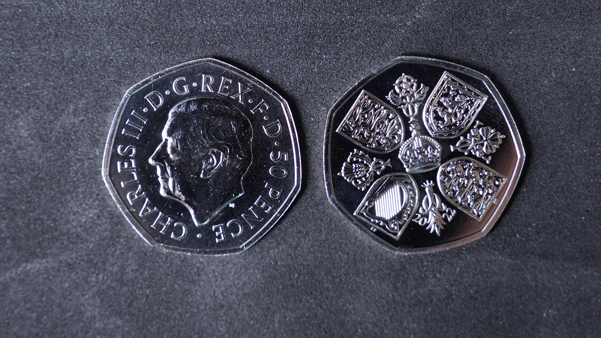 28.10.2022, Großbritannien, Pontyclun: Eine Geldmünze mit dem Konterfei des britischen König Charles III. (l) liegt neben einer Geldmünze, auf der die Rückseite abgebildet ist. Die ersten britischen Geldmünzen mit dem Konterfei des neuen Königs Charles III. kommen in den Umlauf. Die Münzprägeanstalt Royal Mint hat an ihrem Sitz im walisischen Llantrisant mit der Produktion von 50-Pence-Stücken begonnen. Foto: Alistair Heap/PA Wire/dpa - ACHTUNG: Nur zur redaktionellen Verwendung im Zusammenhang mit der aktuellen Berichterstattung und nur mit vollständiger Nennung des vorstehenden Credits +++ dpa-Bildfunk +++