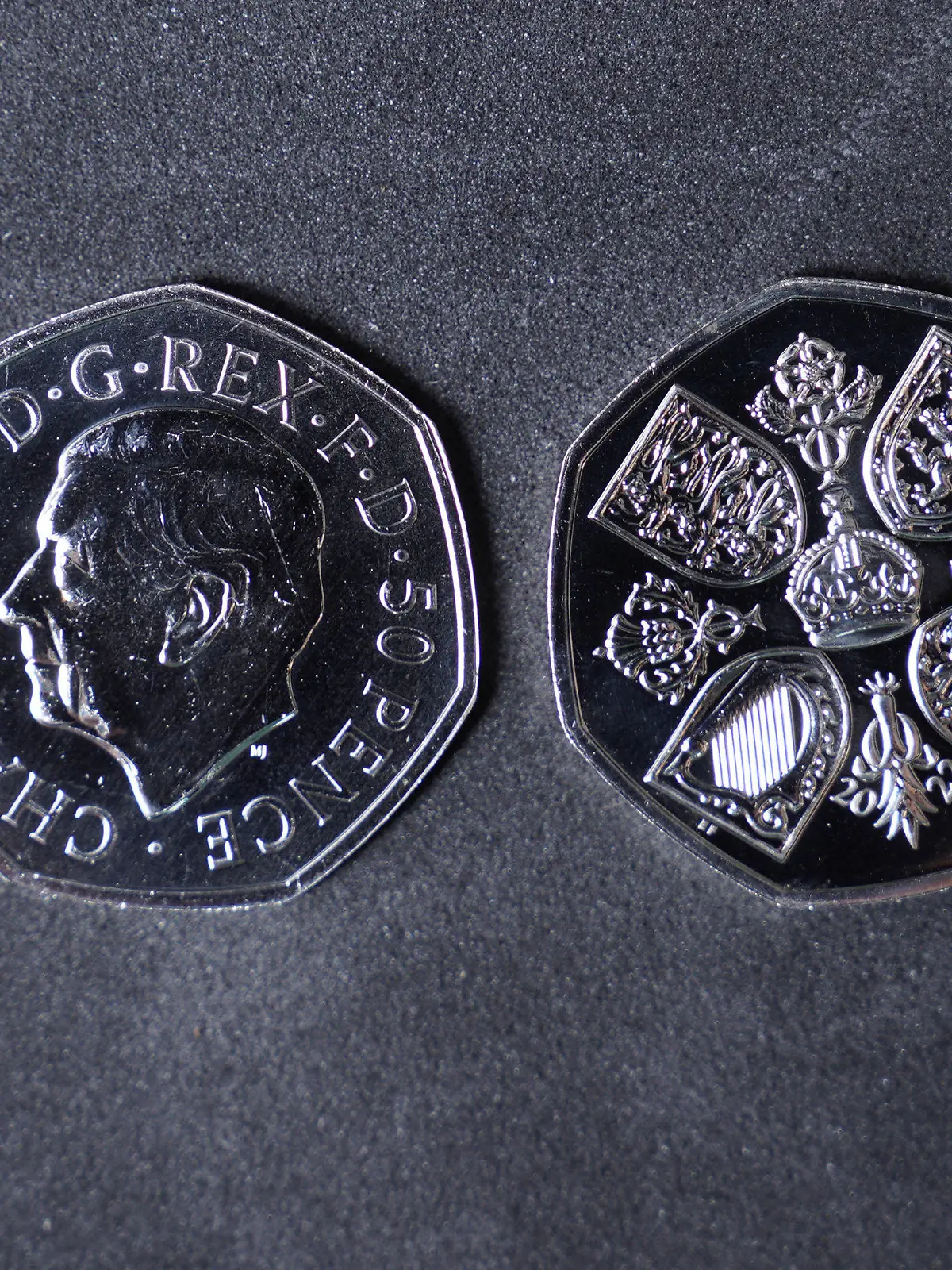 28.10.2022, Großbritannien, Pontyclun: Eine Geldmünze mit dem Konterfei des britischen König Charles III. (l) liegt neben einer Geldmünze, auf der die Rückseite abgebildet ist. Die ersten britischen Geldmünzen mit dem Konterfei des neuen Königs Charles III. kommen in den Umlauf. Die Münzprägeanstalt Royal Mint hat an ihrem Sitz im walisischen Llantrisant mit der Produktion von 50-Pence-Stücken begonnen. Foto: Alistair Heap/PA Wire/dpa - ACHTUNG: Nur zur redaktionellen Verwendung im Zusammenhang mit der aktuellen Berichterstattung und nur mit vollständiger Nennung des vorstehenden Credits +++ dpa-Bildfunk +++