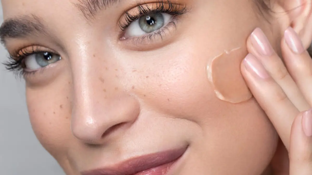 Close up studio shot of a beautiful woman with perfect freckled skin, applying foundation.