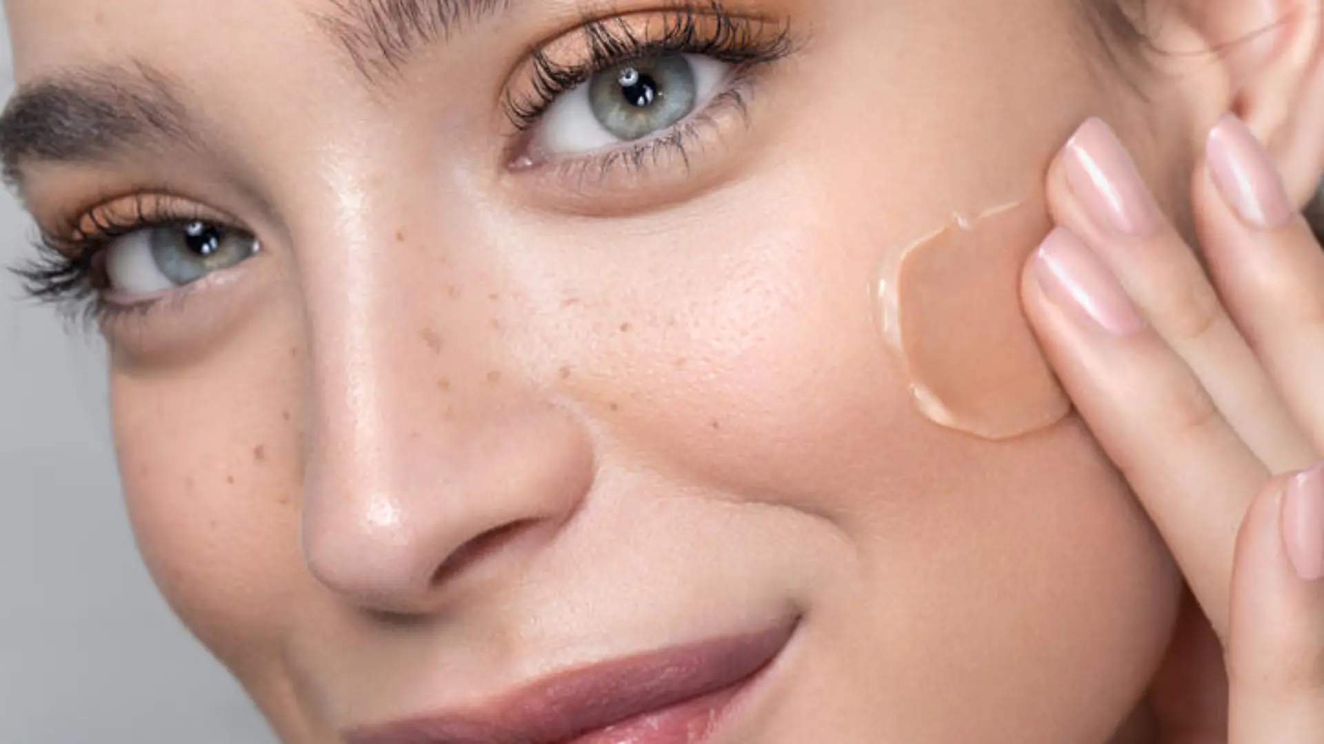 Close up studio shot of a beautiful woman with perfect freckled skin, applying foundation.