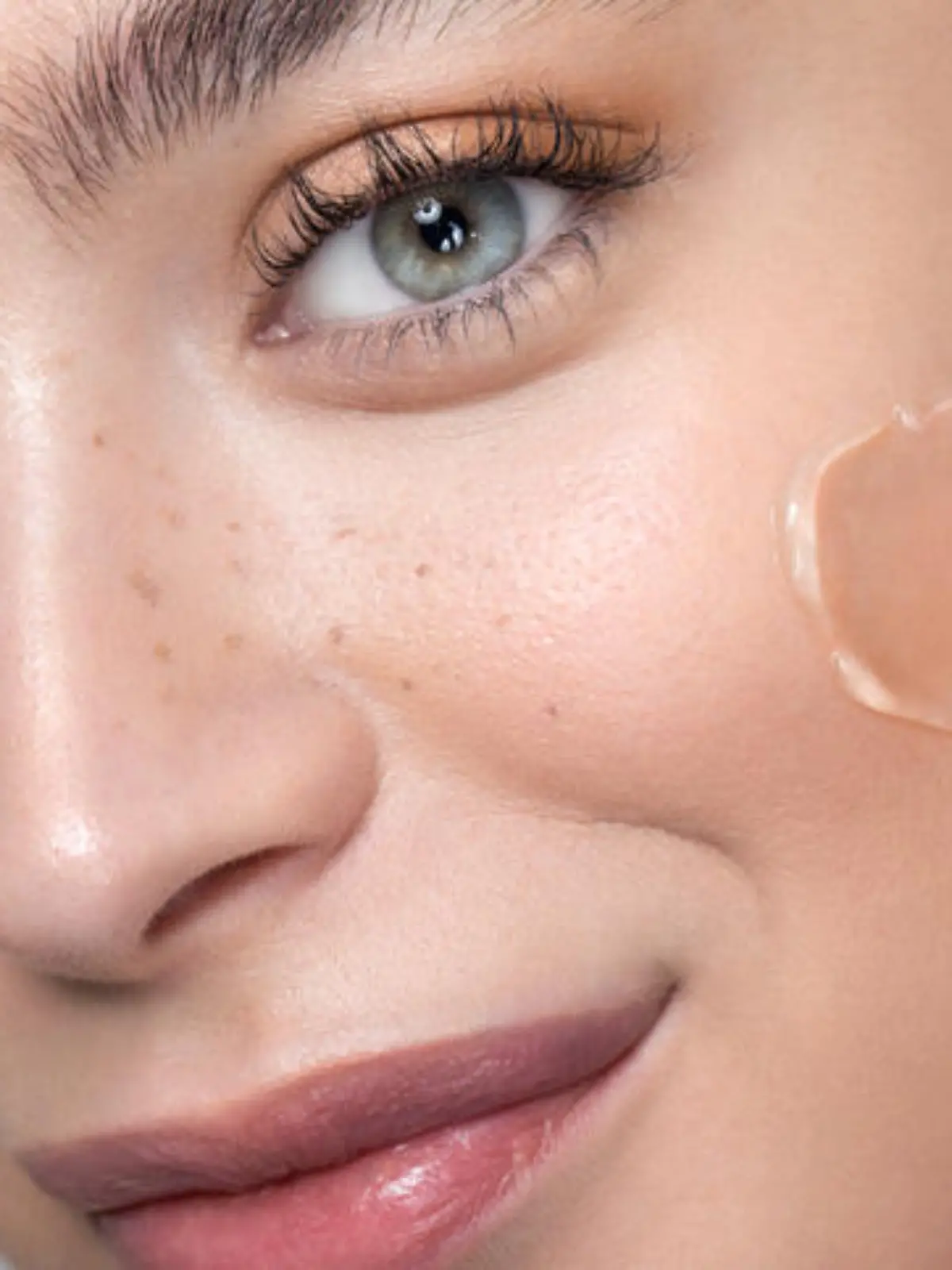 Close up studio shot of a beautiful woman with perfect freckled skin, applying foundation.