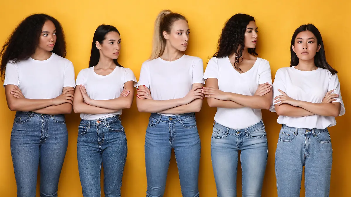 Offended Discontented Multiracial Ladies Looking At Asian Female Friend Unfriendly Disapproving Her Posing Crossing Hands Standing Over Yellow Studio Background. Adult Bullying And Racism