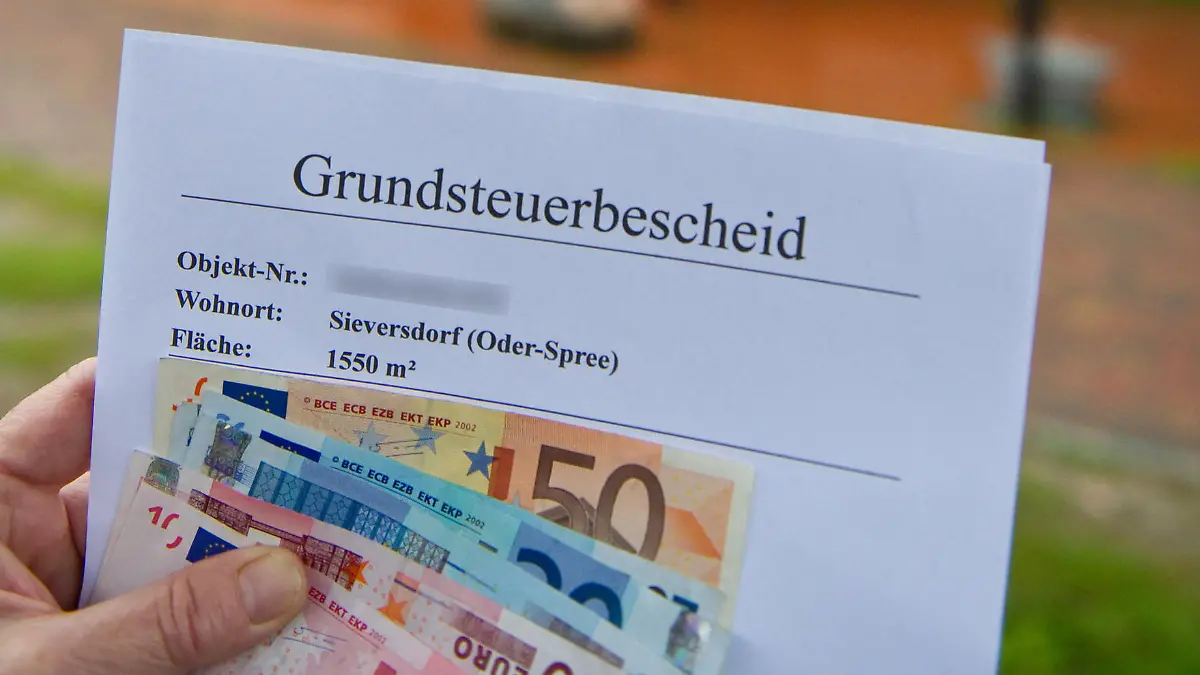 ARCHIV - 09.09.2010, Brandenburg, Sieversdorf: ILLUSTRATION - Eine Frau hält Euro-Geldscheine und einen Grundsteuerbescheid vor ihrem Haus im brandenburgischen Sieversdorf (Oder-Spree) in der Hand (Illustration zum Thema Grundsteuer). Bis Ende Juni seien bei den Finanzämtern rund 1 052 000 Erklärungen eingegangen, teilte das Justizministerium auf Anfrage mit. Damit fehlten immer noch knapp 200 000 Grundsteuererklärungen. (zu dpa: «Grundsteuer: 200 000 Immobilienbesitzern droht Strafzahlung») Foto: Patrick Pleul/dpa-Zentralbild/dpa +++ dpa-Bildfunk +++