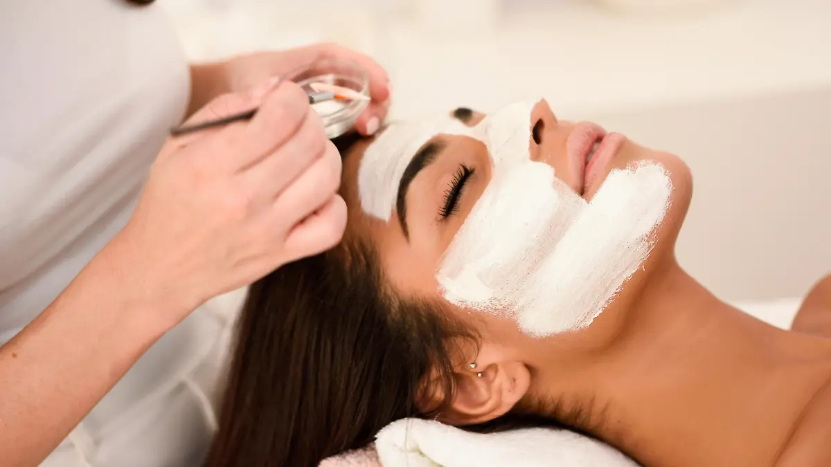 Aesthetics applying a mask to the face of a beautiful woman in modern wellness center. Beauty and Aesthetic concepts.
