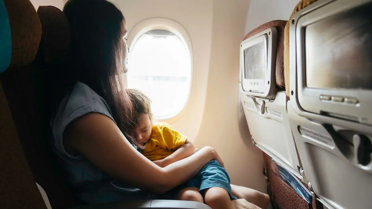 Baby sleeps in mom's arms while on an airplane in flight.