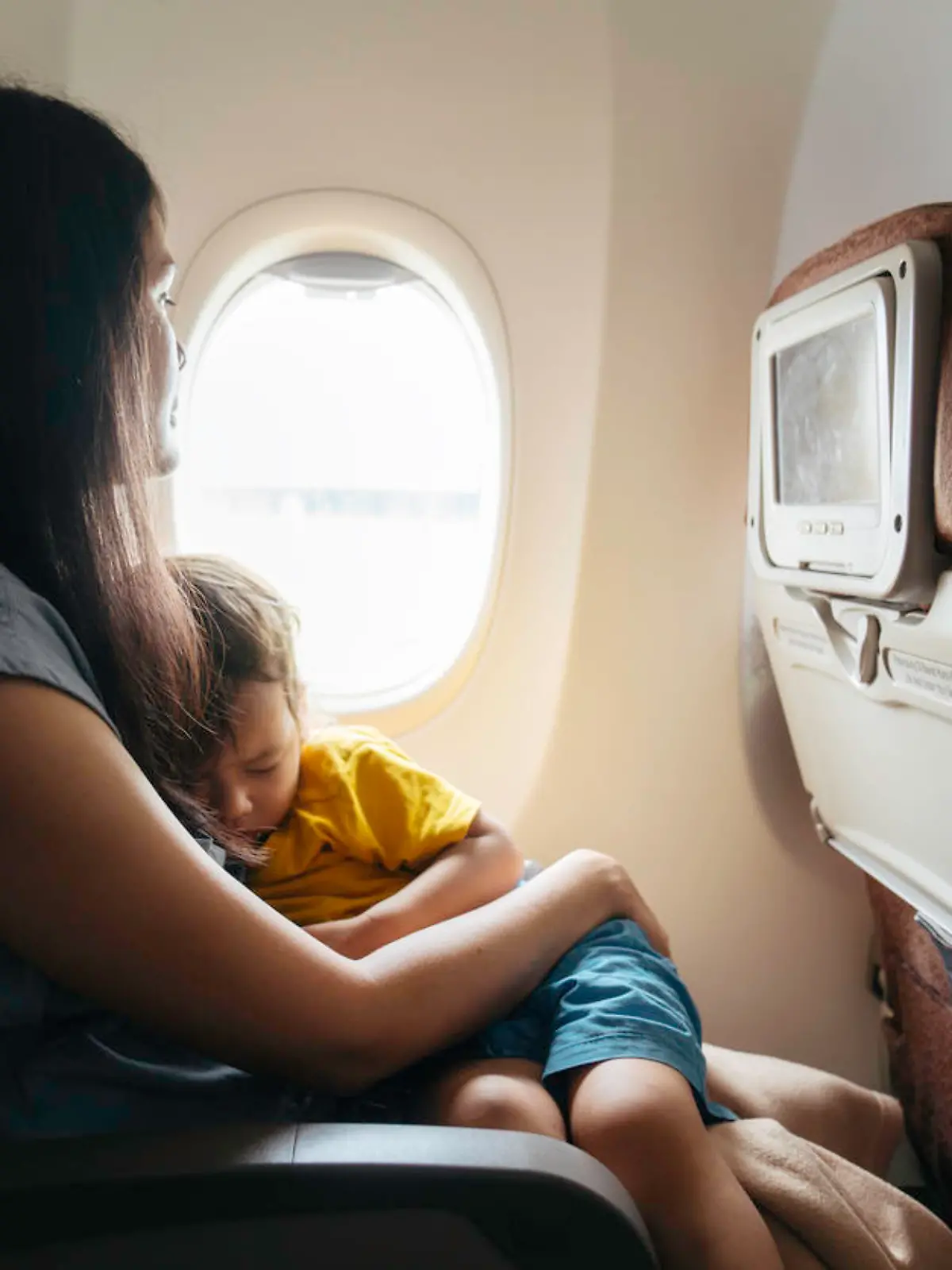 Baby sleeps in mom's arms while on an airplane in flight.