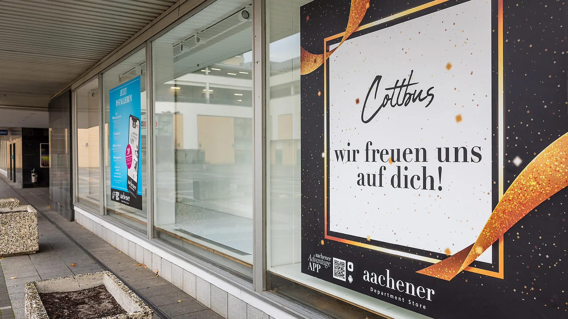 An einem Schaufenster des noch nicht eröffneten Modehauses «Aachener» hängt ein Imageplakat. Das Modehaus folgt in Cottbus auf die am 30. Juni 2023 geschlossene Filiale von «Galeria Kaufhof» - der Eröffnungstermin wurde in letzter Zeit immer wieder verschoben und steht aktuell noch nicht fest.