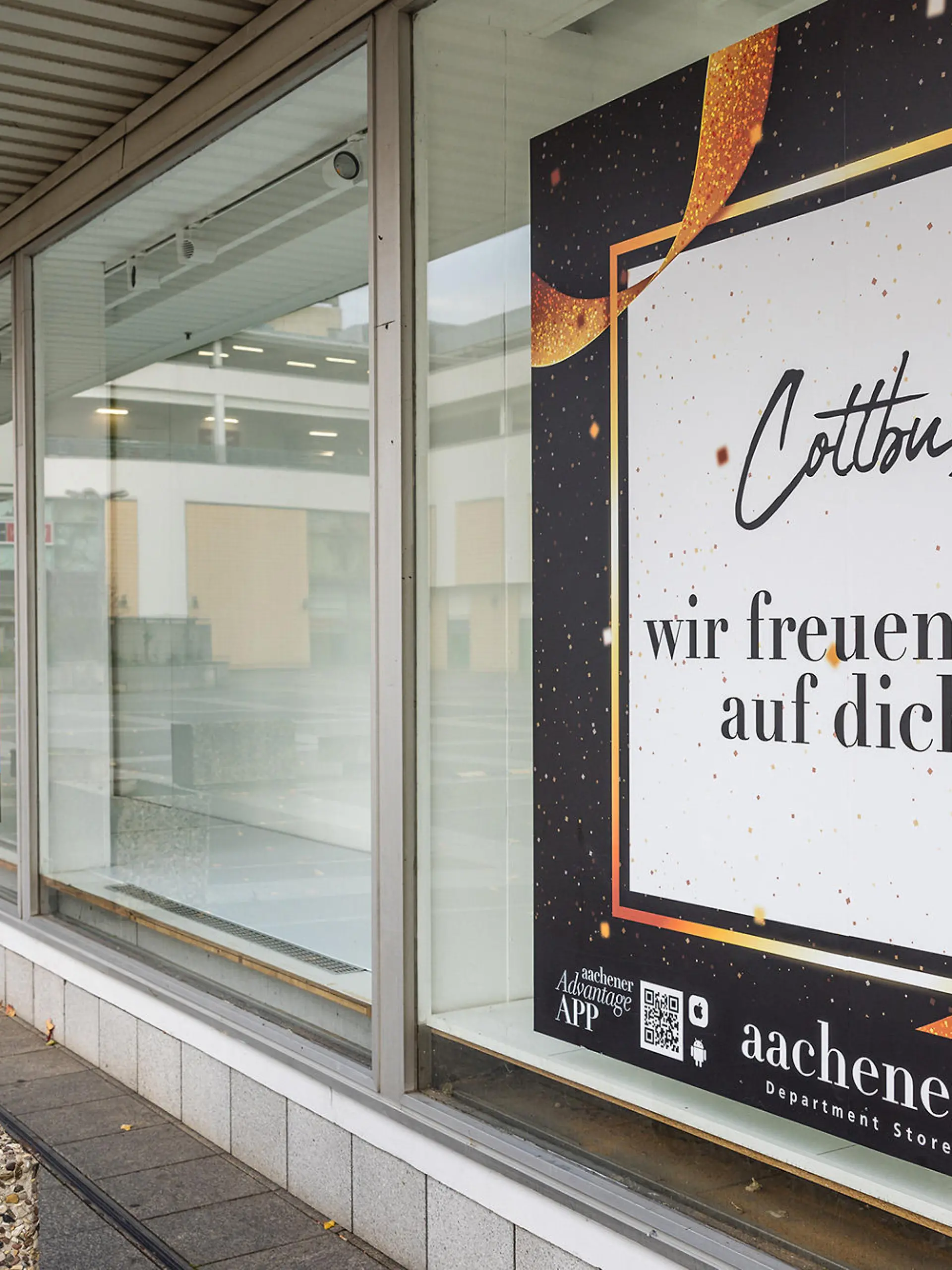 An einem Schaufenster des noch nicht eröffneten Modehauses «Aachener» hängt ein Imageplakat. Das Modehaus folgt in Cottbus auf die am 30. Juni 2023 geschlossene Filiale von «Galeria Kaufhof» - der Eröffnungstermin wurde in letzter Zeit immer wieder verschoben und steht aktuell noch nicht fest.