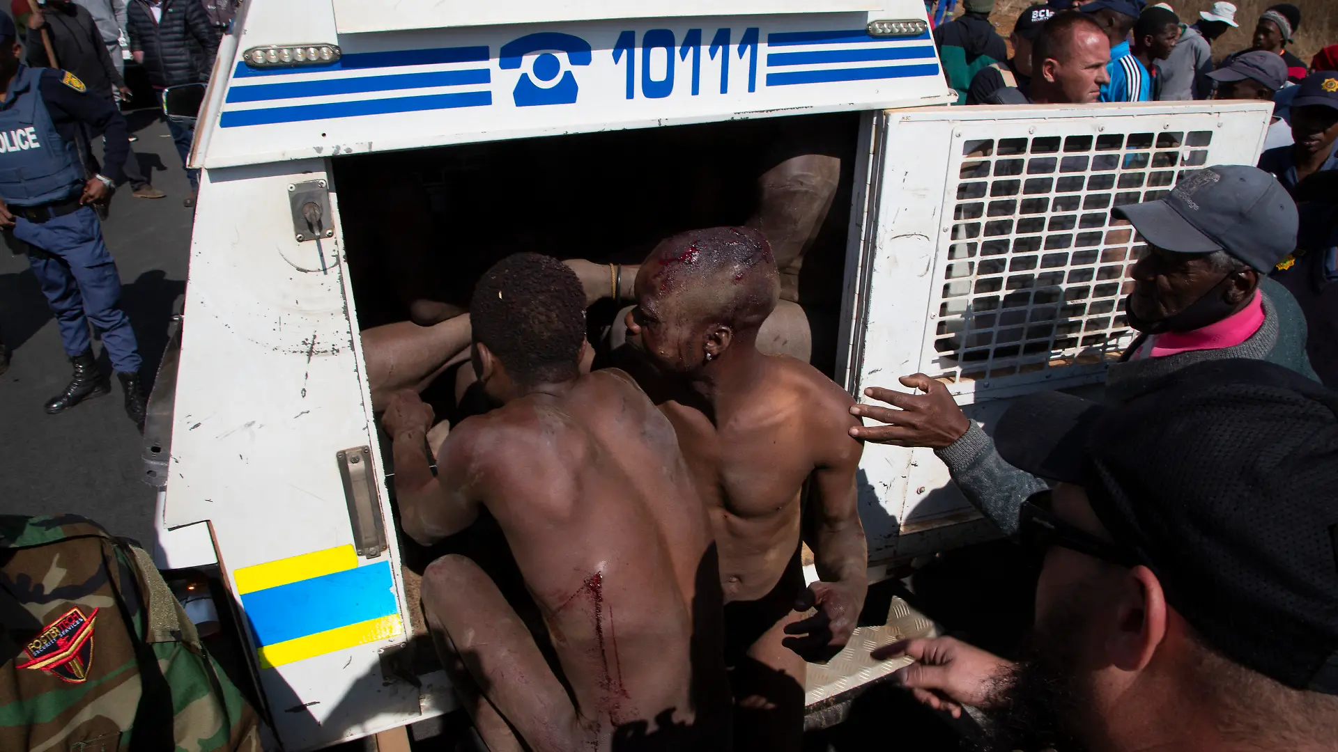 Illegal gold miners are placed in a police van after community members beat them and stripped them naked before handing over to police near Krugersdorp, South Africa, Thursday, Aug. 4, 2022. Community members beat suspected illegal miners with sticks and set fire to their camps following the alleged gang rapes of eight women by miners last week. (AP Photo/Denis Farrell)