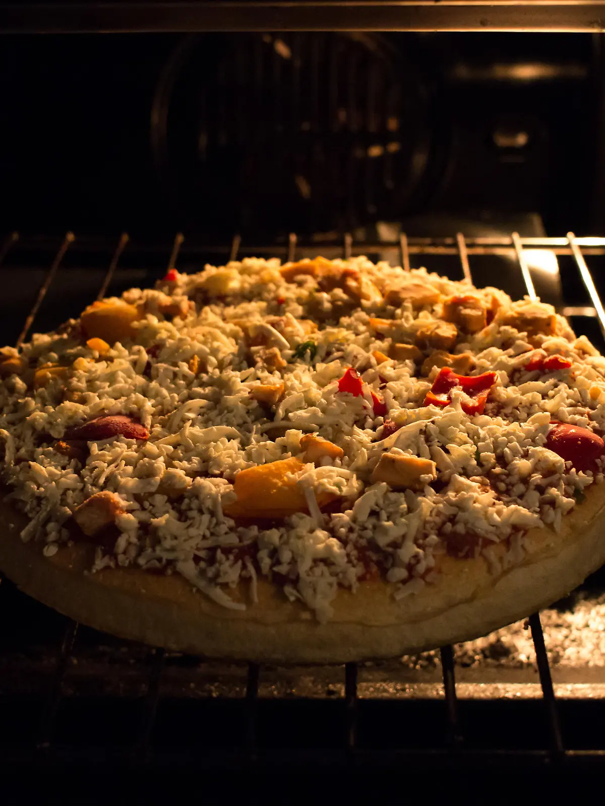 A frozen pizza just went in the hot oven, still frozen and almost ready to eat.