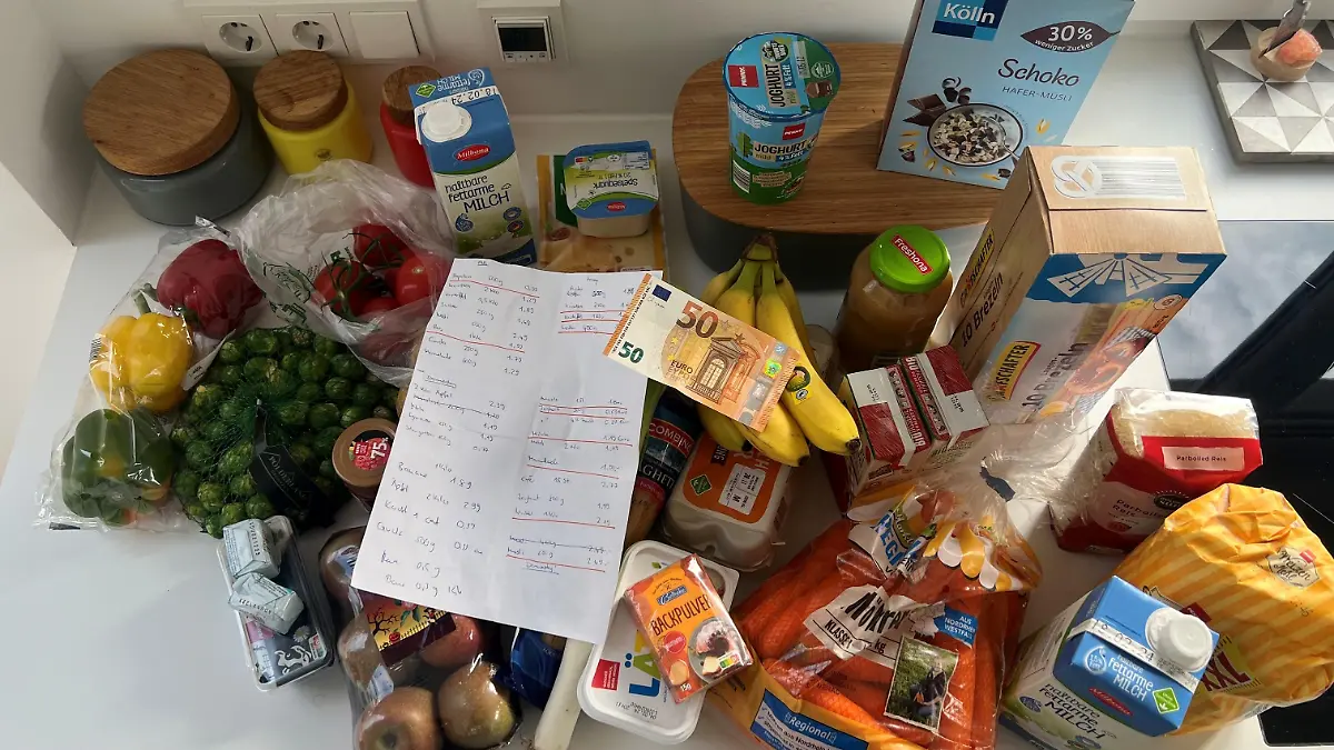 Die eingekaufen Lebensmittel liegen stehen auf einem Tisch. Darauf der Einkaufszettel und ein 50-Euro-Schein.