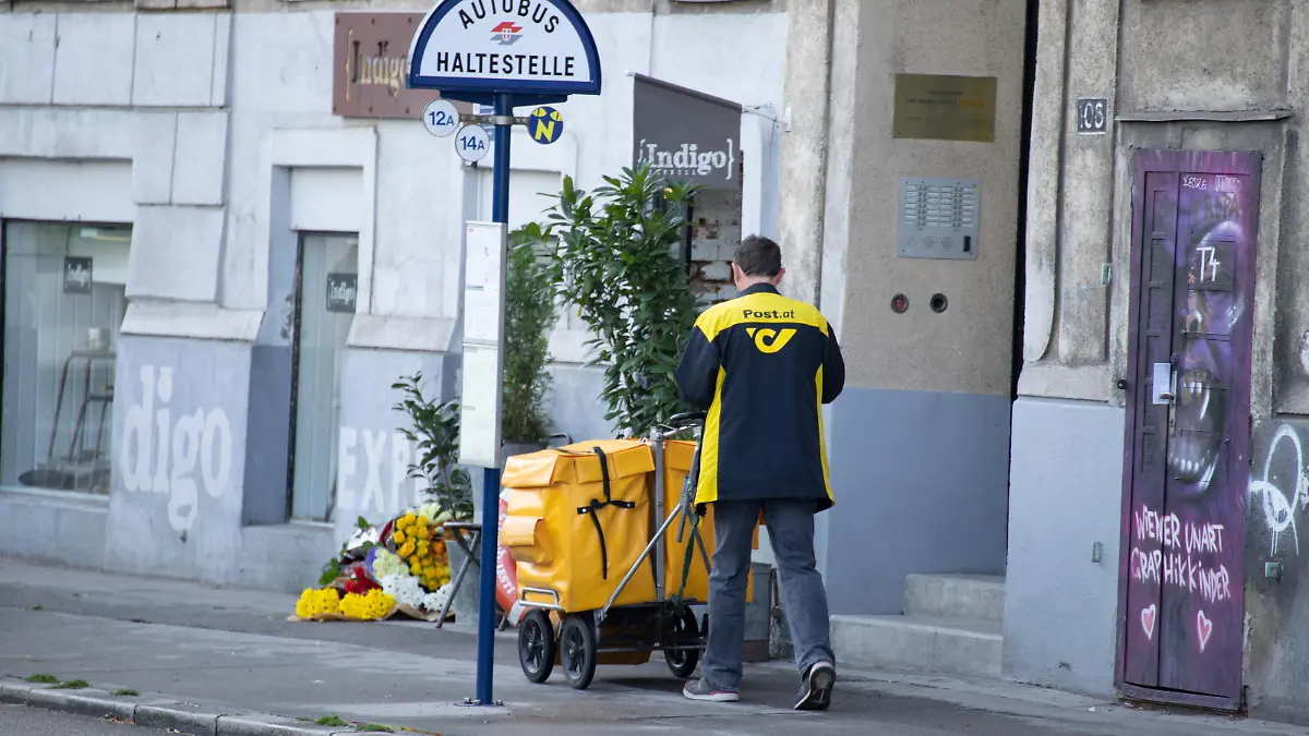 Ein Briefträger der Post fährt mit einem Transportwagen am Gehsteig. Er trägt eine Jacke mit gelbem Logo und Schriftzug der Post. Wien, Österreich. August 2020 - 20200805_PD9797 || Mindestpreis 20 Euro 