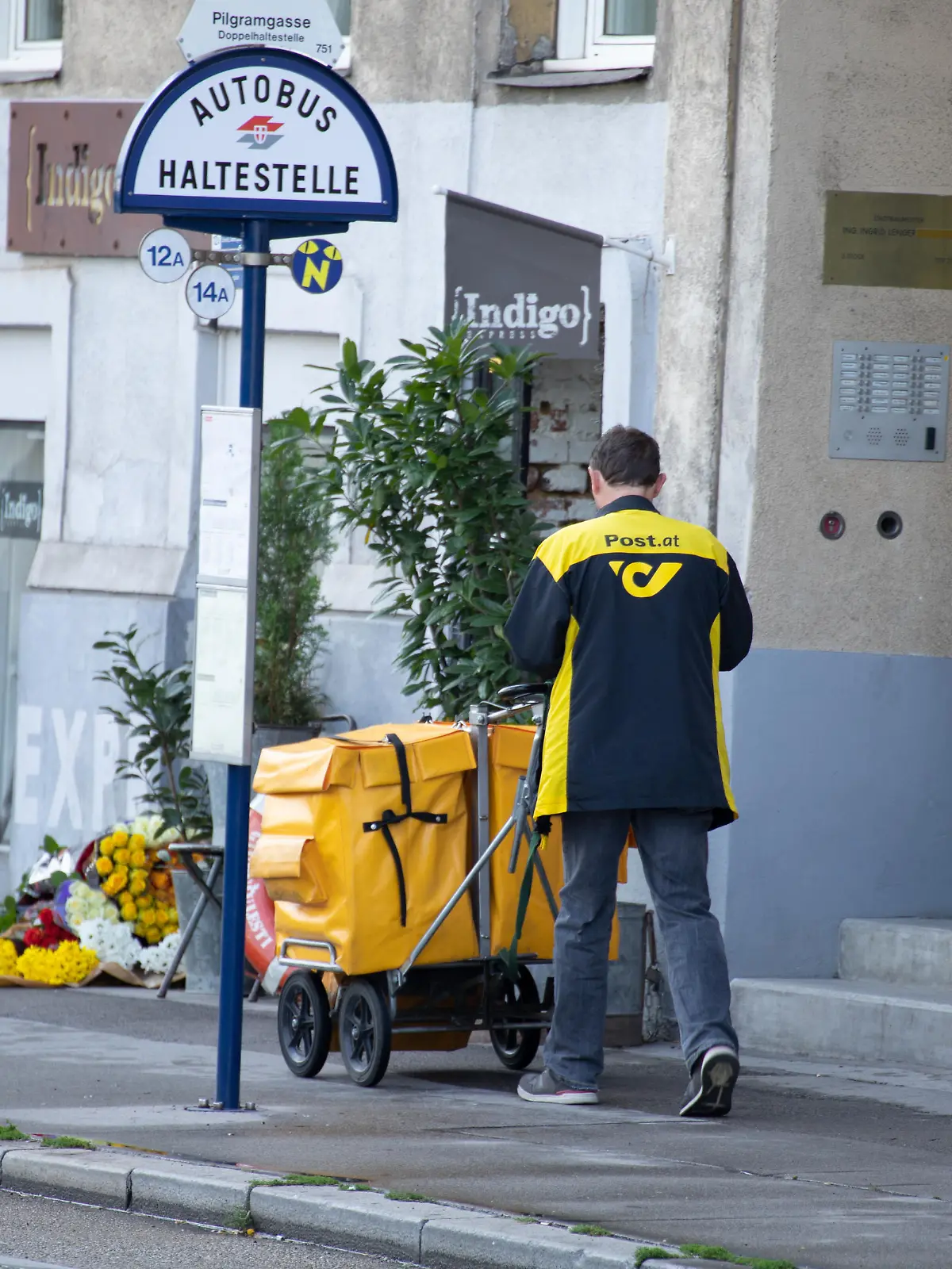 Ein Briefträger der Post fährt mit einem Transportwagen am Gehsteig. Er trägt eine Jacke mit gelbem Logo und Schriftzug der Post. Wien, Österreich. August 2020 - 20200805_PD9797 || Mindestpreis 20 Euro 