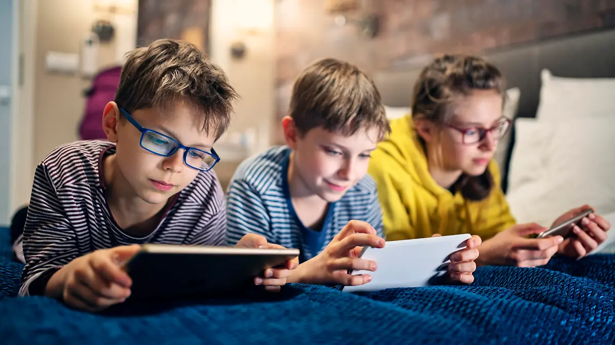 Three kids are lying on bed and playing with modern mobile devices - tablets and smartphone.
Nikon D850